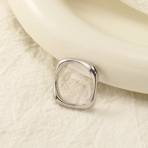 Macro shot of polished silver geometric square ring on a cream textured fabric background