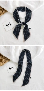 Detail of a slim black scarf with white stripes and soft pink edges on a woven mat