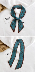 Detail of teal twilly scarf with brown polka dots tied in a bow on a white linen surface