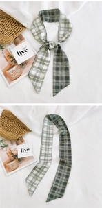 Detail of green and white checkered silk scarf styled as a headband on white fabric