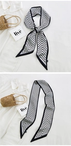 Detail of long black and white geometric V-pattern silk scarf tied on a straw bag handle
