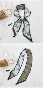 Close-up of a floral print twilly silk scarf with dark green edges and cursive script