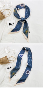 Detail view of a long navy blue silk scarf with gold zodiac signs on a white shirt