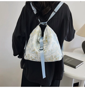 Detail of a white backpack featuring blue butterfly prints and a wide adjustable strap