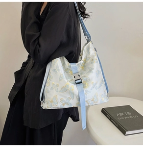 Side view of floral butterfly print shoulder bag with light blue strap on a model
