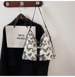 Detail of white tote bag with black and gold butterfly print and metallic buckle