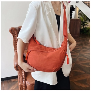 Detail van oranje nylon tas met gevlochten rits gedragen door model in wit kostuum