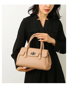 Detail of crocodile embossed leather handbag with woven handles and twist-lock closure