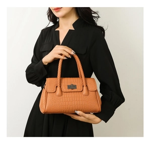 Detail of crocodile pattern brown handbag with woven handle and metal twist lock