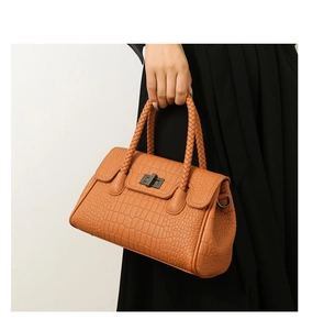 Detail of orange-brown crocodile embossed handbag with woven handle and metal twist lock