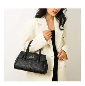 Detail of black crocodile-embossed handbag featuring woven handles and metal turn-lock
