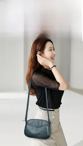 Model wearing a deep cyan pebbled leather crossbody bag with a curved flap and zipper