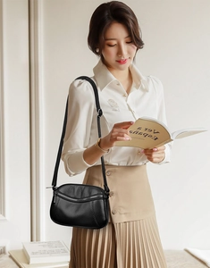Detail of black lychee grain leather crossbody bag with silver zipper on elegant model