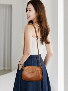 Side view of a brown pebbled leather crossbody bag worn by a model in a warm interior