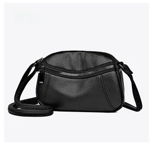 Detail of black pebbled leather crossbody bag with curved zipper compartment and long strap