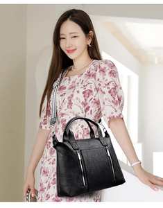 Detail of black pebbled leather tote bag featuring dual zippers and wide geometric strap