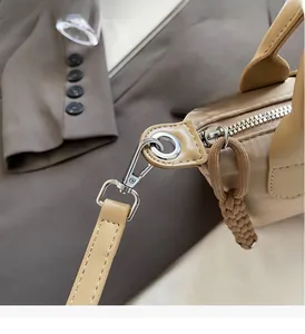 Detail of silver metal zipper and woven puller on beige minimalist dumpling bag