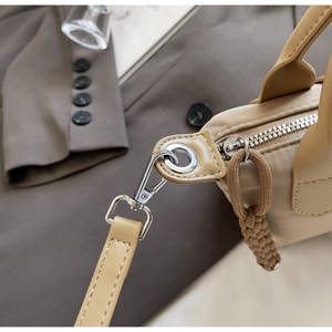 Detail of khaki nylon crossbody bag featuring silver metal D-rings and braided rope zippers