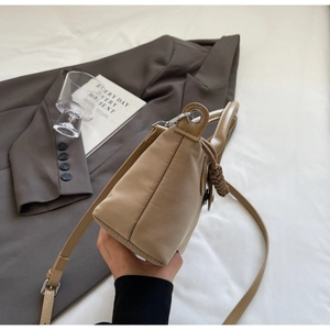 Side view of khaki nylon crossbody bag with cotton-padded texture and woven charm