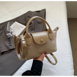 Detail of beige PU leather handbag with top handle, crossbody strap and woven charm
