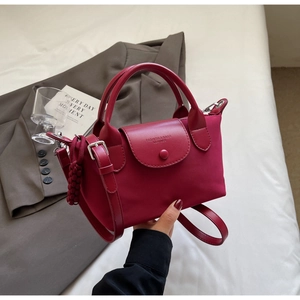 Detail of burgundy dumpling bag with leather strap and woven ball charm on white fabric