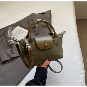 Detail of olive green nylon handbag featuring leather trim and woven pendant charm