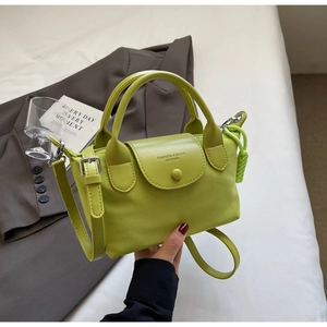 Close-up of green leather handbag with handle, shoulder strap and side woven charm