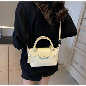 Detail view of cream nylon mini crossbody bag with embossed logo and woven knot charm