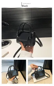 Mini black glossy crossbody bag with handles and shoulder strap in a modern setting