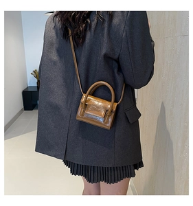 Détail d'un mini sac à main en cuir verni caramel porté sur un blazer gris foncé