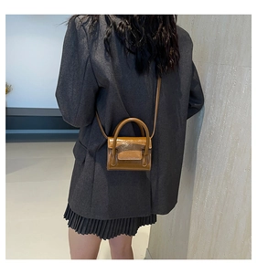 Gros plan d'un mini sac bandoulière en cuir verni marron porté avec un costume gris