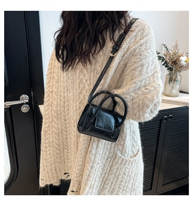 Gros plan du mini sac en cuir verni noir avec poignées anneaux sur pull en tricot