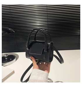 Mini sac à main en cuir verni brillant noir tenu à la main avec bandoulière fine