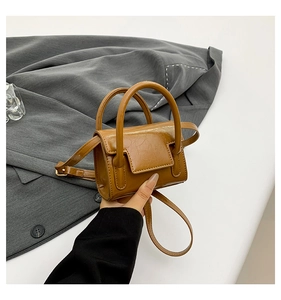 Détail du mini sac à main carré marron sur costume gris montrant la texture du cuir