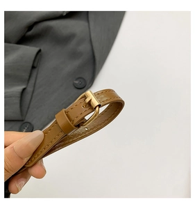 Détail de ceinture fine en similicuir marron avec une boucle en métal doré poli