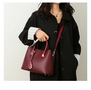 Model wearing a burgundy pebble leather tote bag with gold hardware and shoulder strap
