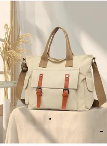 Detail of beige canvas tote bag with brown fabric handles and dual buckle front pocket