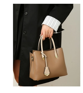 Detail of a brown leather tote bag with snakeskin handles and golden metal hooks