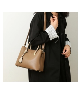 Modern camel tote bag with leather braided handles shown on a model in a trench coat