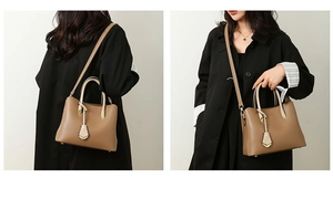 Detail of taupe litchi grain leather tote bag with gold leaf pendant on black coat