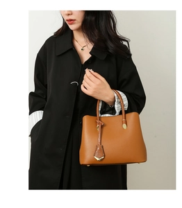 Brown leather tote bag with lychee texture and crocodile tag on a black coat model