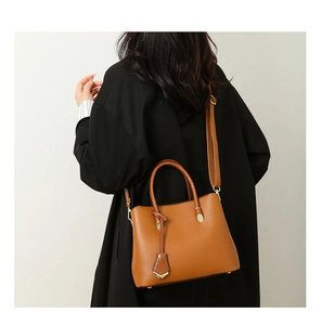 Close-up of camel lychee pattern tote bag with gold hardware worn with a long black coat