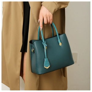 Close-up of green tote bag with crocodile texture handles and gold metal hardware