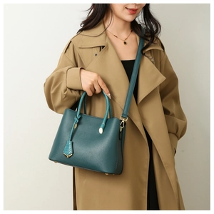 Close-up of peacock green pebble leather tote with gold hardware on khaki trench coat