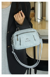 Close-up of a light blue textured women bag with three zippers and a wide grey strap
