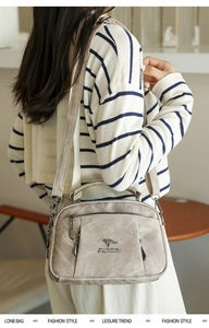 Detail of light brown leather crossbody bag featuring dual zippers and kangaroo logo