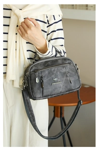Deep grey kangaroo logo handbag worn by a model with multi-zippered compartments