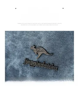 Detail of blue denim fabric texture and black kangaroo metal logo on a stylish handbag