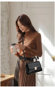 Black crocodile embossed leather handbag with gold clasp worn by a woman in elegant setting