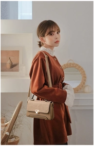 Detail of beige handbag with crocodile embossed flap and gold twist lock in lifestyle setting